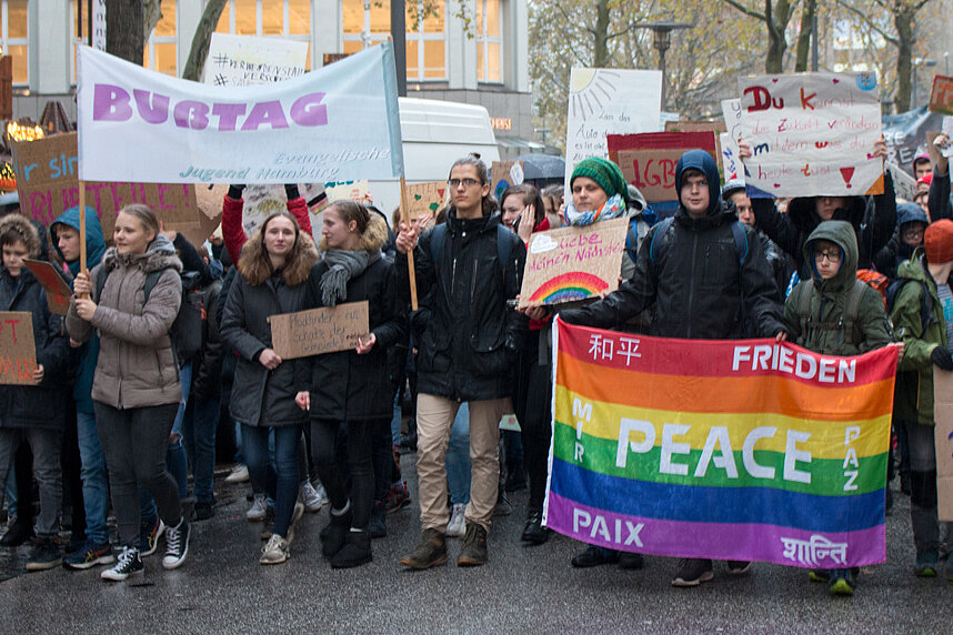 Zahlreiche junge Menschen am Anfang eines Demonstrationszuges. Sie tragen Plakate und Banner mit Aufschriften wie beispielsweise: Peace, Busstag, Umweltschutz.